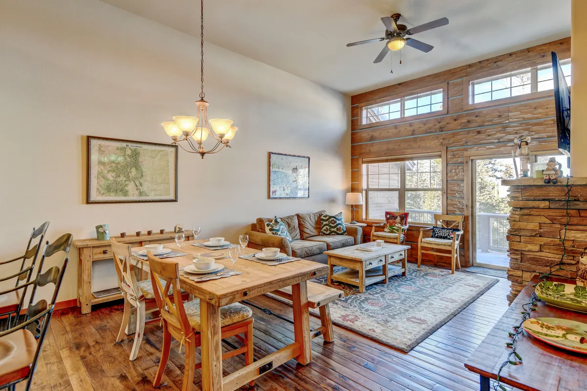 An inviting space featuring a dining table set for a meal, a comfortable sofa, warm wooden accents, and large windows that bathe the room in sunlight. The area exudes a sense of togetherness and relaxation, encouraging communal gatherings.