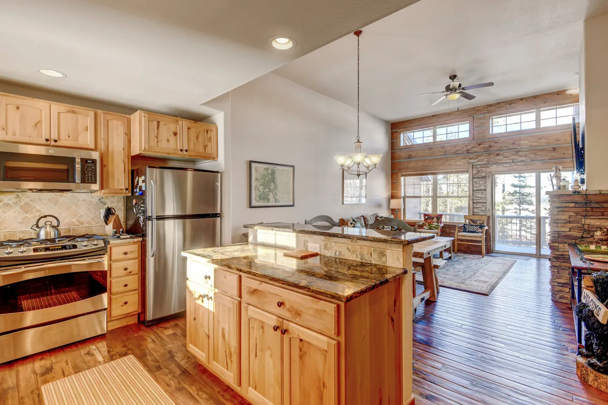 A bright, open kitchen and dining area with a central island, sleek cabinetry, a dining table, and expansive windows offering scenic views. The setup is ideal for socializing, cooking, and enjoying morning coffee while taking in the outdoors.