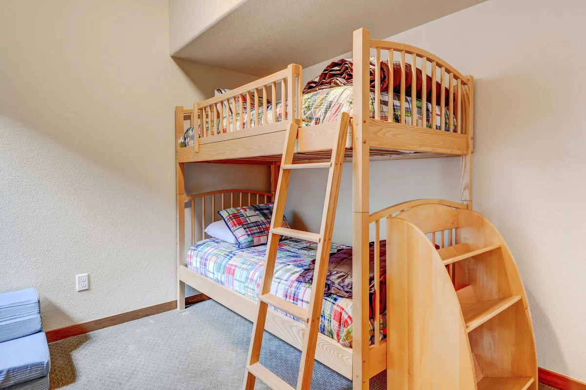 A playful bunk room with twin-over-twin bunk beds, plaid bedding, and a sturdy wooden ladder. The room is bright and inviting—ideal for children to play, sleep, and share stories.