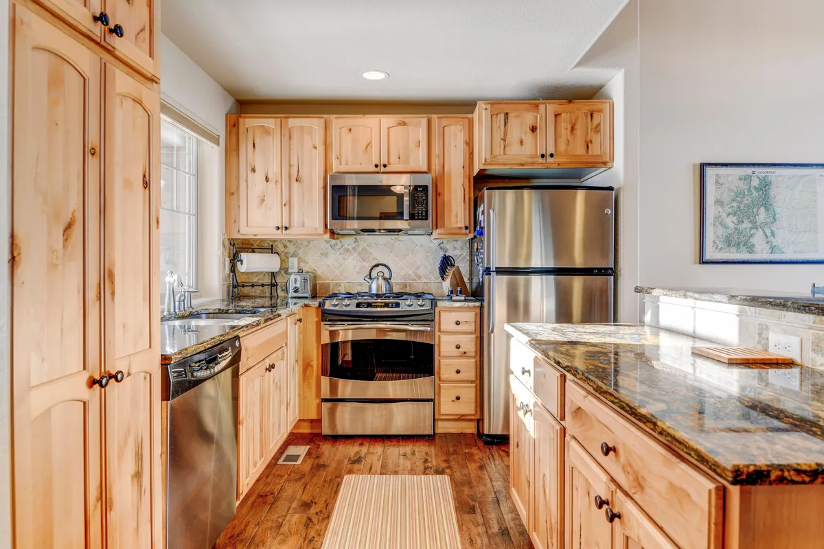 A warm and inviting kitchen with wooden cabinetry, granite countertops, and premium stainless steel appliances. Natural light pours in through a nearby window, enhancing the cozy ambiance. The setup is ideal for cooking, entertaining, and enjoying family time.