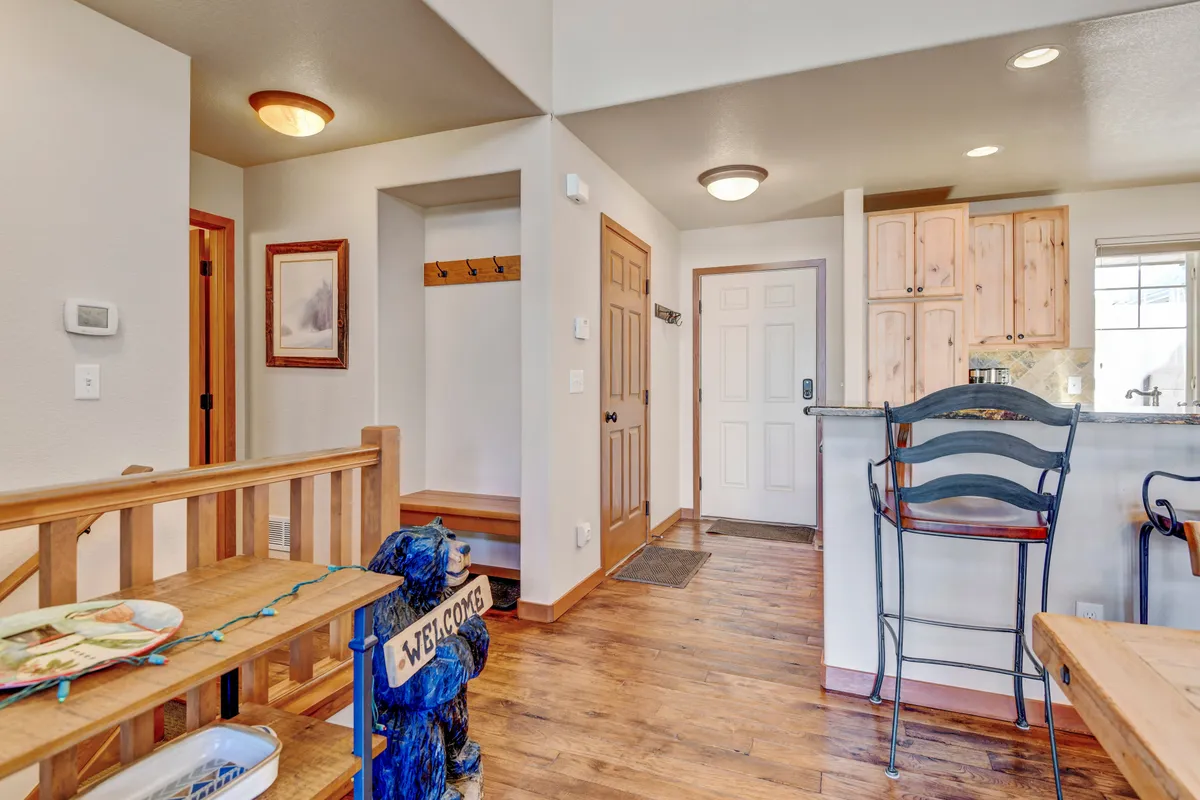A welcoming entryway featuring a wooden bench, bar stools, a welcome sign, coat hooks, and framed artwork. The space is designed for greeting guests and storing outerwear or gear, hinting at an organized, inviting transition area between adventure and relaxation.