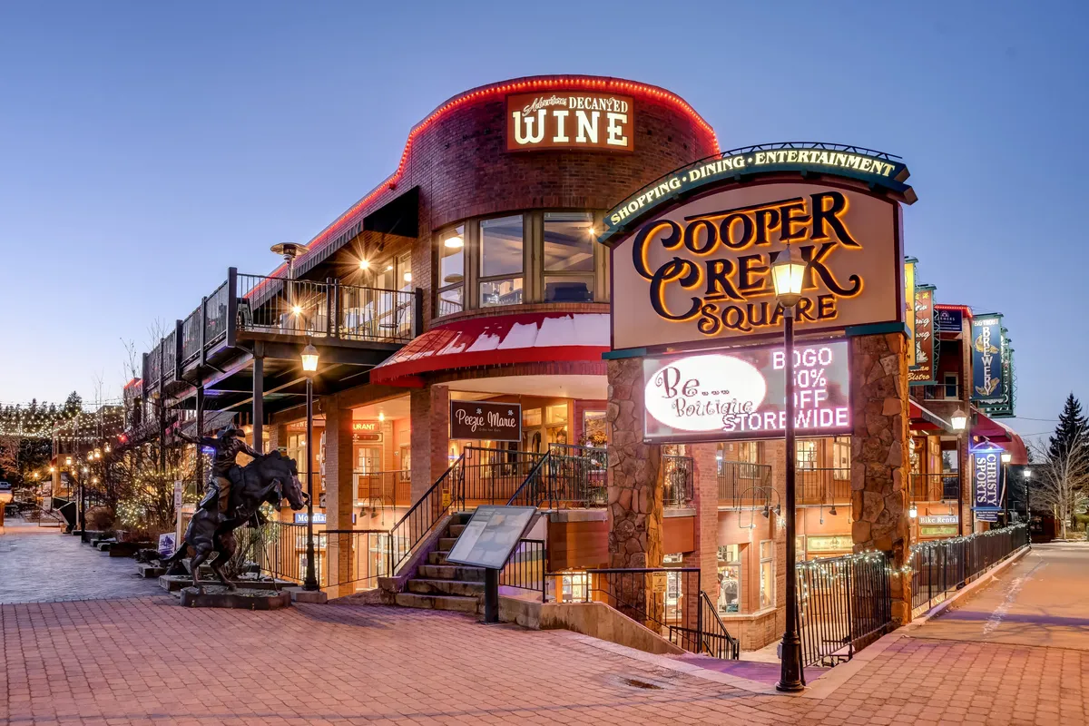 An exterior shot of the lively Cooper Creek Square with signs, decorative wine elements, and outdoor seating. The festive, welcoming atmosphere suggests access to premium shopping, dining, and local entertainment—key components of a year-round luxury experience.