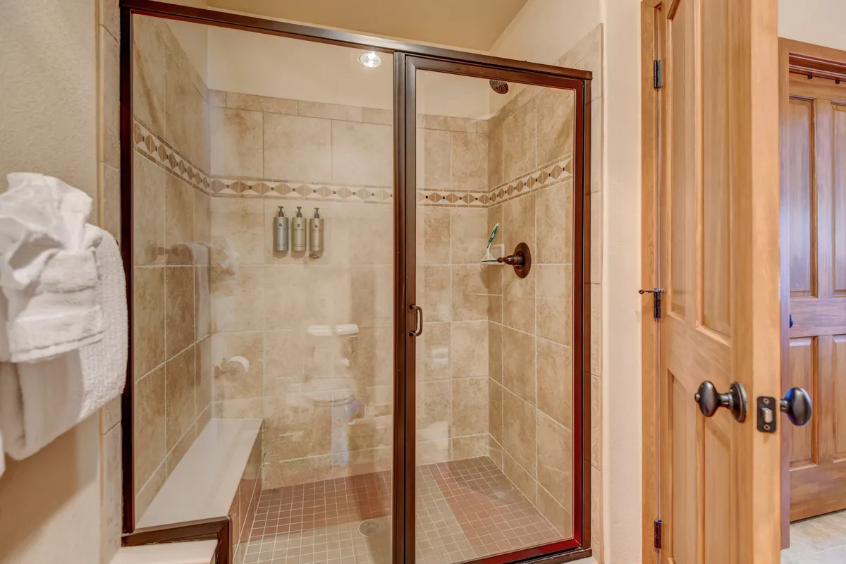A spa-like bathroom with a glass shower enclosure, textured tiles, fluffy white towels on a towel rack, and a wooden door. The space feels calm, rejuvenating, and sophisticated.